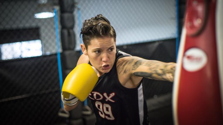 Woman wearing boxing gloves is aiming her glove at a punching bag